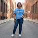 Person wearing a blue  Edwin Allen 'Champions' t-shirt on a city street. EAHS Edwin Allen High School Blue Tee - Champion & Crest Front - Unisex T-Shirt