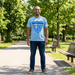 Man wearing a light blue  Edwin Allen high school official merch t-shirt with 'Champions' design in a park EAHS Edwin Allen High School Blue Tee - Champion & Crest Front - Unisex T-Shirt