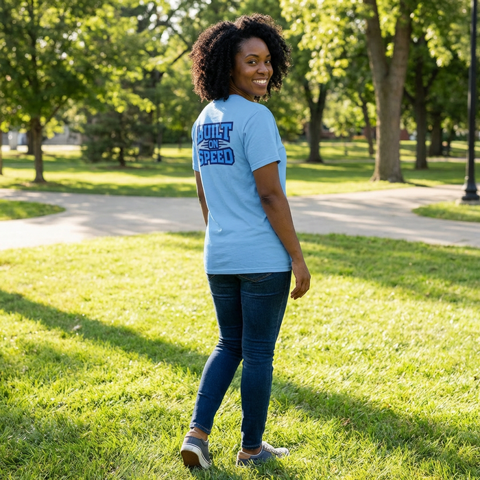 Woman wearing a light blue t-shirt with text in a park EAHS Edwin Allen Blue Tee - Crest Front - Built on Speed Back - Unisex T-Shirt