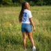 Woman in a white t-shirt and denim shorts standing in a grassy field with wildflowers. EAHS Unisex Microfiber T-Shirt - White